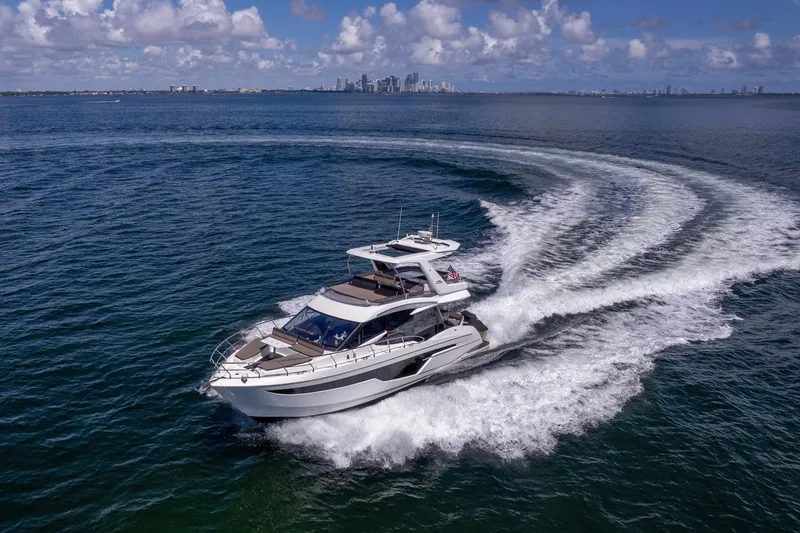 Slide: The Image of 2021 Galeon 500 Fly yacht cruising on open water with city skyline in background. - 5