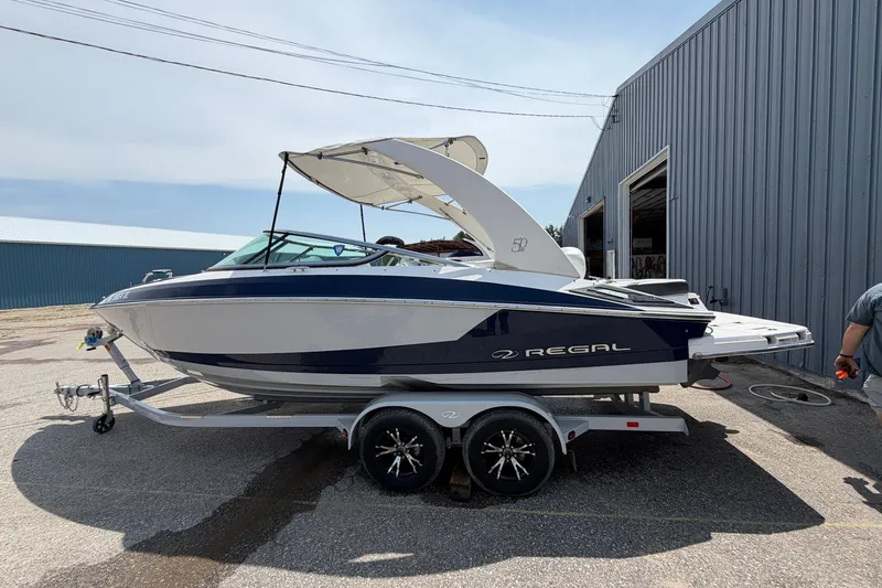 The Image of 2020 Regal 2300 Bowrider boat on trailer, parked beside a metal building. - 0