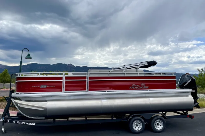 The Image of 2026 Sun Tracker Fishin' Barge 22 DLX pontoon boat on trailer, cloudy sky backdrop. - 0