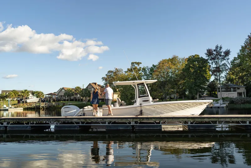 Slide: The Image of 2026 Sea Hunt Ultra 275 Coffin Box boat docked with two people onboard, scenic waterfront. - 63