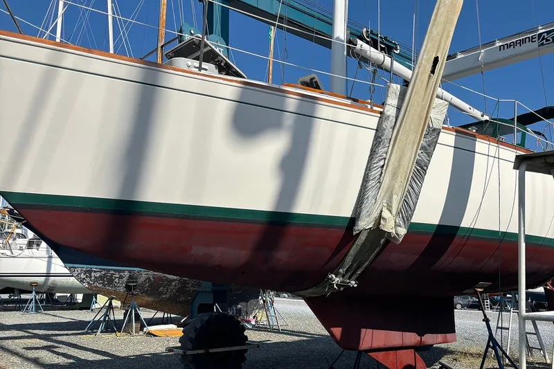 Slide: The Image of 1983 Sabre 38 sailboat on stands, hull visible, in a boatyard under clear blue sky. - 11