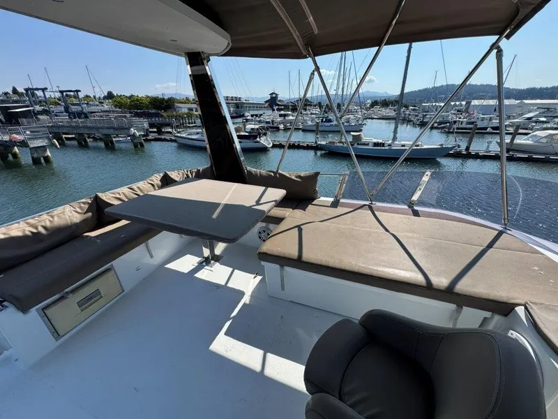 Slide: The Image of The image shows the deck of a 2016 Fountaine Pajot Motor Yacht 37. There are cushioned seating areas and a table. A marina with several boats is visible in the background. - 48