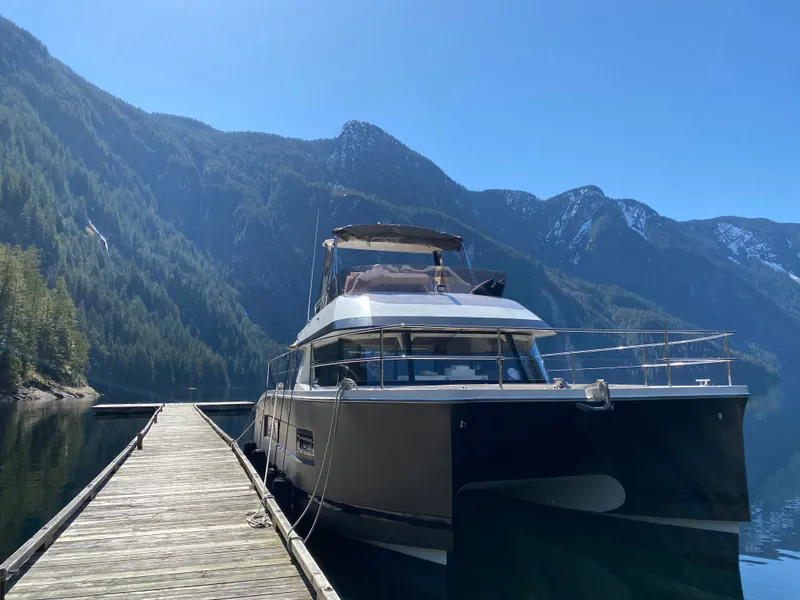 Slide: The Image of A 2016 Fountaine Pajot Motor Yacht 37 docked at a wooden pier with a mountainous backdrop. - 1