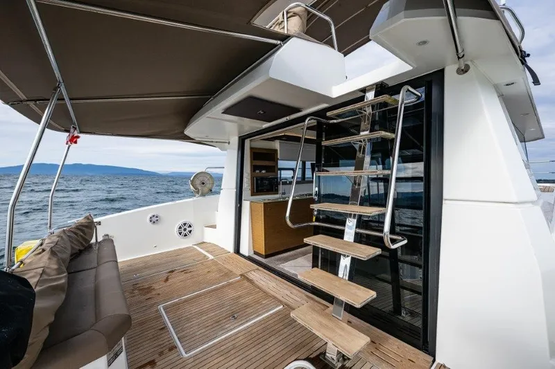 Slide: The Image of The image shows the aft deck of a 2016 Fountaine Pajot Motor Yacht 37. There's a staircase to the upper level and a bench seat on the deck. - 6
