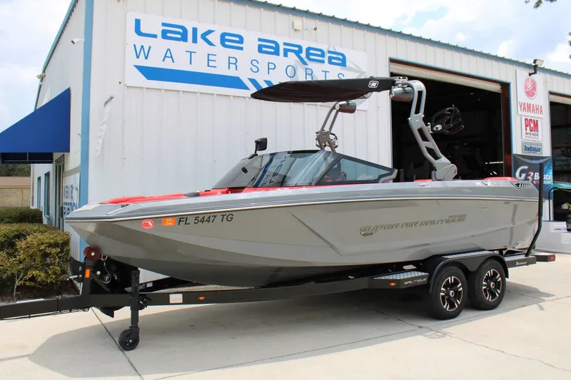 Slide: The Image of A gray 2021 Super Air Nautique GS22 boat on a trailer in front of a building labeled "Lake Area Watersports." - 2
