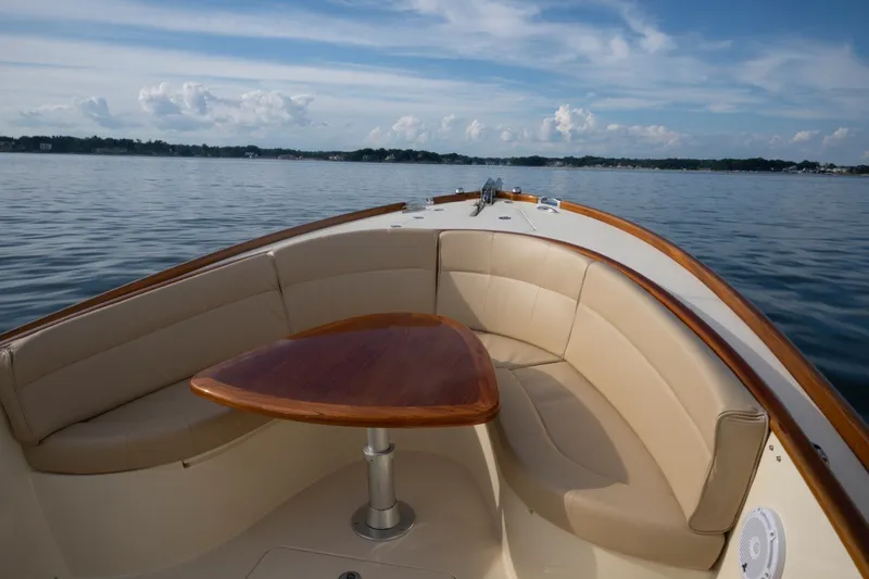 Slide: The Image of 2014 Hinckley Talaria 29C boat interior with cushioned seating and wooden table on calm water. - 12