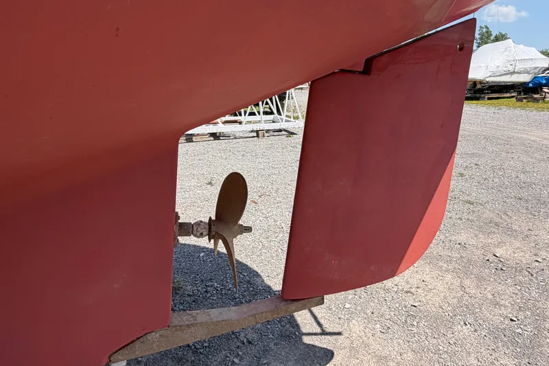 Slide: The Image of Rear view of a 2000 Island Packet 320 sailboat's propeller and rudder on gravel. - 15