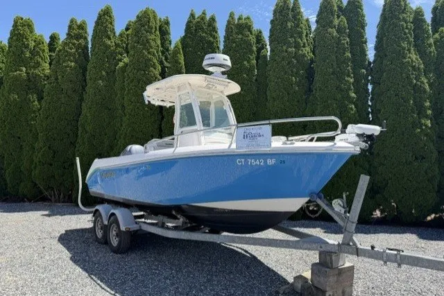 The Image of 2013 Everglades 210 Center Console boat on trailer, parked near tall trees. - 0