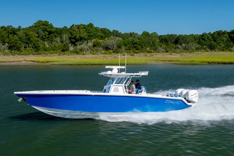 Slide: The Image of 2022 Blackwater 36 Sport boat cruising on a serene lake with lush green shoreline. - 54