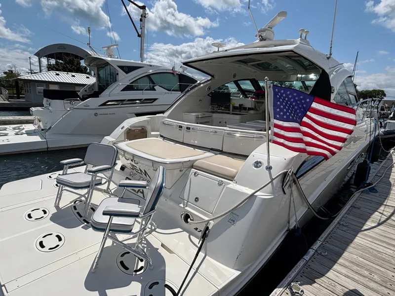 Slide: The Image of A 2012 Sea Ray 470 Sundancer docked. It features a spacious aft deck with chairs and an American flag. - 2