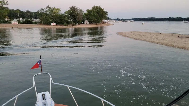 Slide: The Image of A boat navigates calm waters near a sandy shoreline with trees in the background. - 40