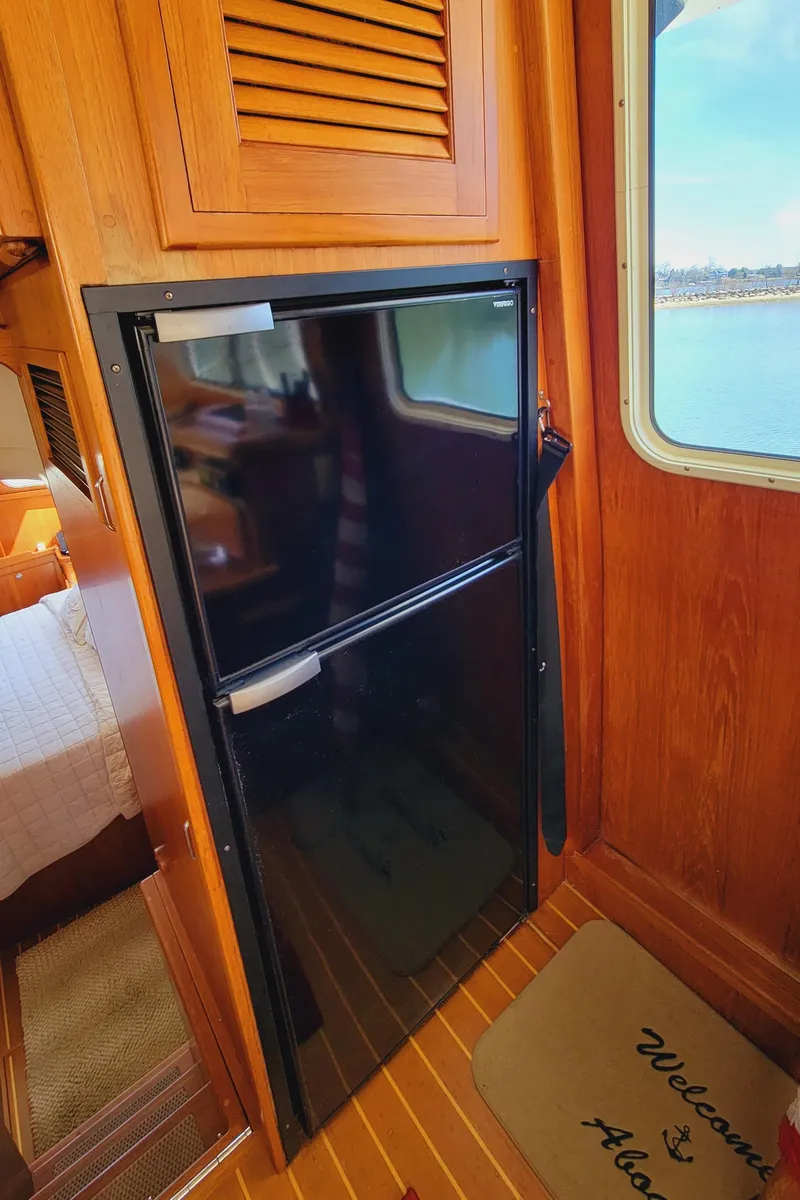 Slide: The Image of A compact refrigerator in a wooden interior with a 'Welcome Aboard' mat beside it. - 26