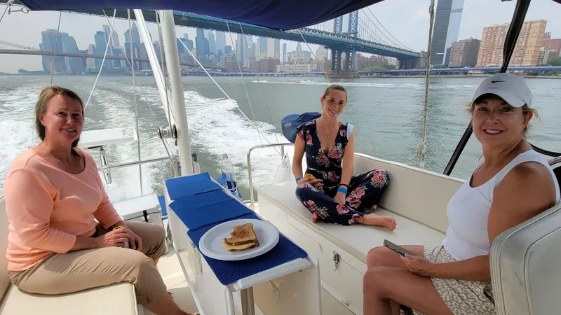 Slide: The Image of Three women sit on a boat with a city skyline and bridge in the background. - 11