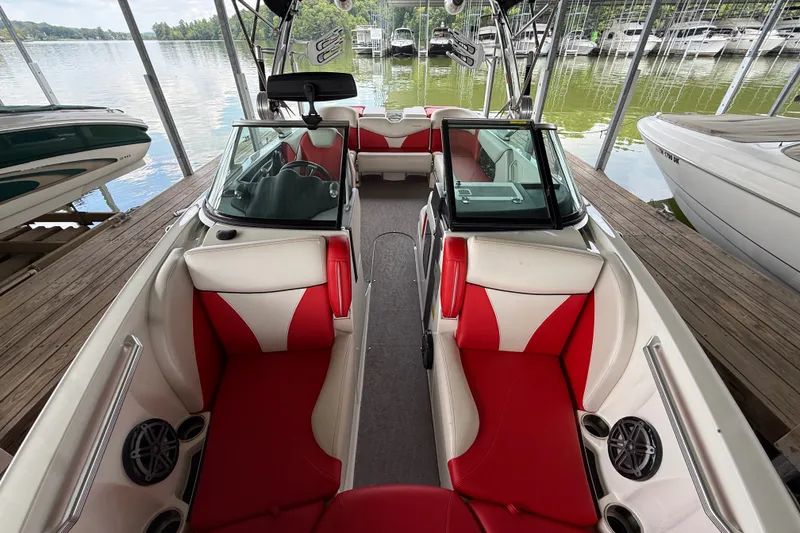 Slide: The Image of 2017 MasterCraft X23 boat interior with red and white seating, docked by the lake. - 23