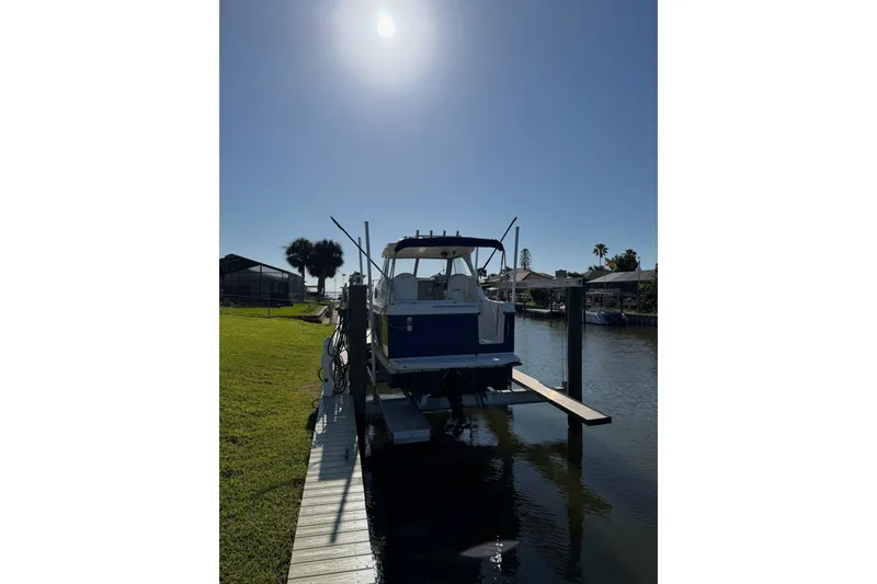 Slide: The Image of 2009 Bayliner Discovery 246 docked under bright sun, near waterfront homes. - 17