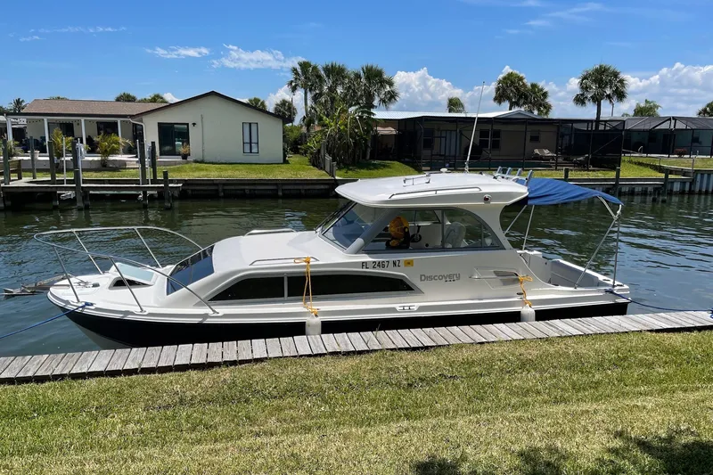 The Image of 2009 Bayliner Discovery 246 boat docked by a canal, sunny day, waterfront homes in background. - 0