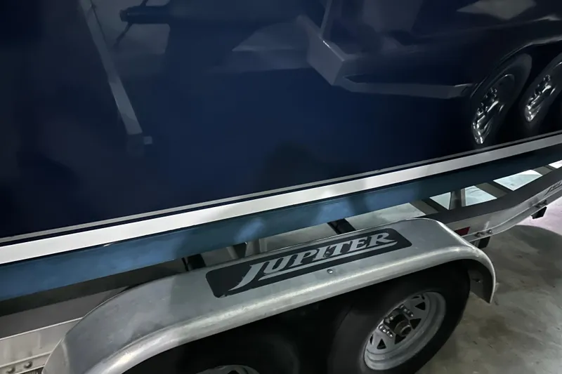 Slide: The Image of 2013 Jupiter 26 FS boat on trailer, showcasing sleek blue hull and logo. - 2