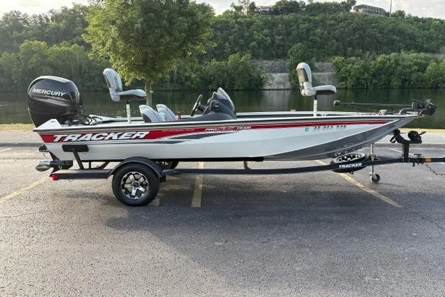 The Image of 2018 Tracker Pro Team 195 TXW boat on trailer by a scenic river. - 1