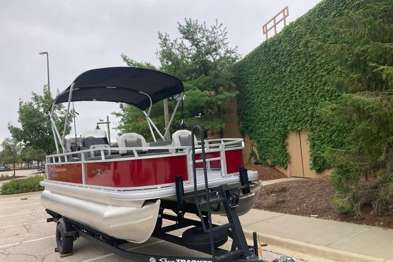 Slide: The Image of 2026 Sun Tracker Bass Buggy 18 DLX pontoon boat on trailer, parked near greenery. - 7