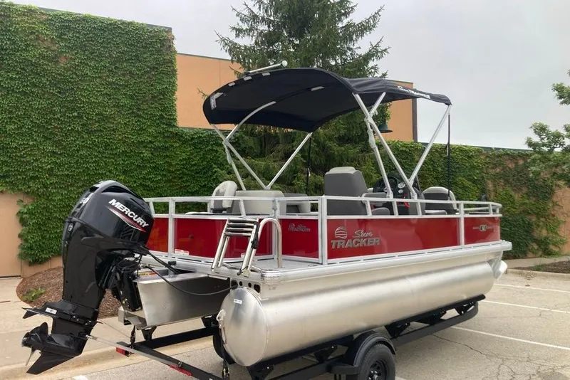 Slide: The Image of 2026 Sun Tracker Bass Buggy 18 DLX pontoon boat with Mercury engine, parked outdoors. - 6