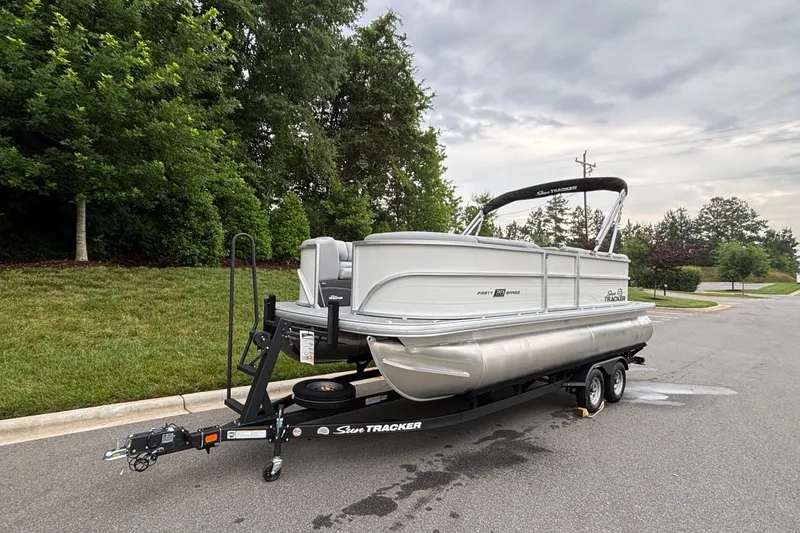 Slide: The Image of 2026 Sun Tracker Party Barge 20 DLX pontoon boat on trailer, parked on a suburban street. - 2
