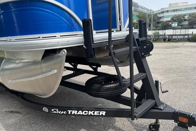 Slide: The Image of 2026 Sun Tracker Party Barge 18 DLX on trailer, featuring blue exterior and sturdy pontoons. - 9