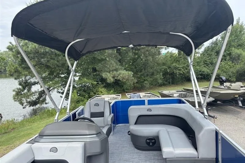 Slide: The Image of 2026 Sun Tracker Party Barge 18 DLX pontoon boat with canopy, docked near a scenic lake. - 18