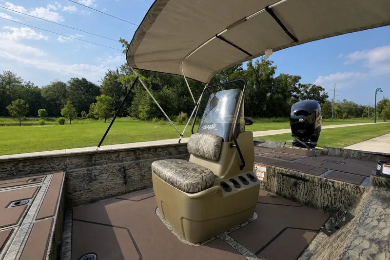 Slide: The Image of 2026 Tracker Grizzly 2072 CC boat interior with camo seating and canopy, set in a lush green landscape. - 2