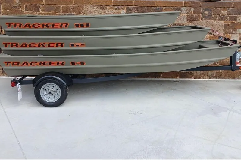 Slide: The Image of Stacked Tracker Grizzly 10 Jon boats on trailer, 2026 model, against brick wall. - 2