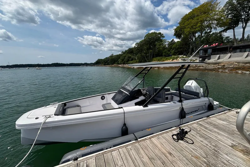 Slide: The Image of 2022 Axopar 22 T-Top boat docked by a scenic shoreline under a partly cloudy sky. - 2