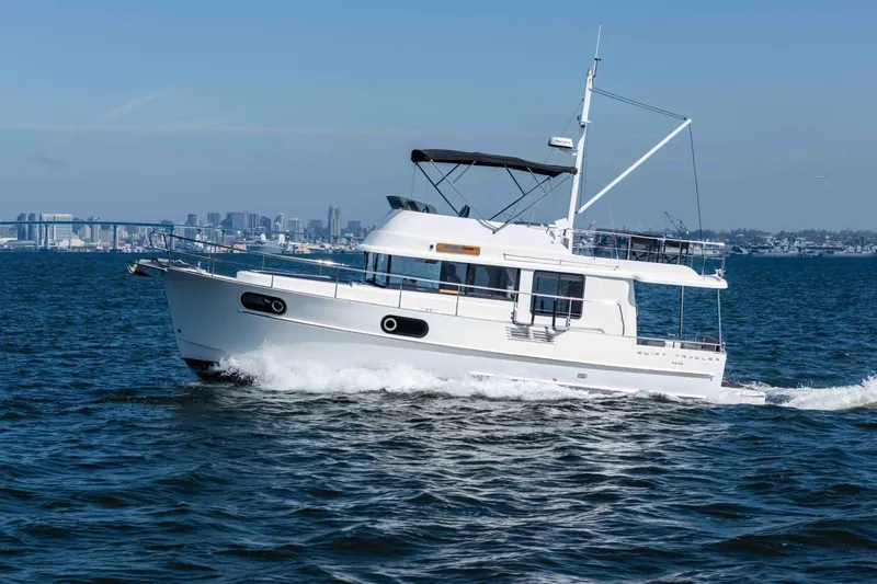 Slide: The Image of 2019 Beneteau Swift Trawler 44 cruising on open water with city skyline backdrop. - 1