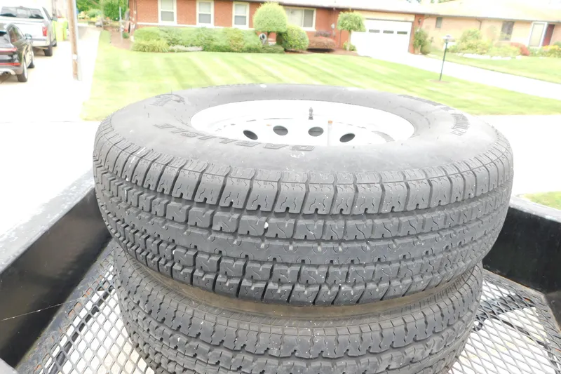 Slide: The Image of Two stacked tires on a metal trailer with suburban houses in the background. - 89