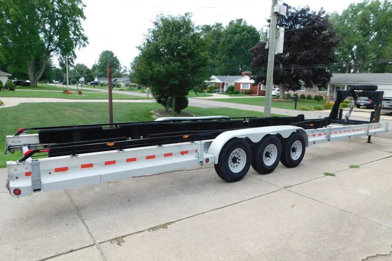 Slide: The Image of Triple-axle boat trailer parked on a suburban driveway, surrounded by green lawns and trees. - 81