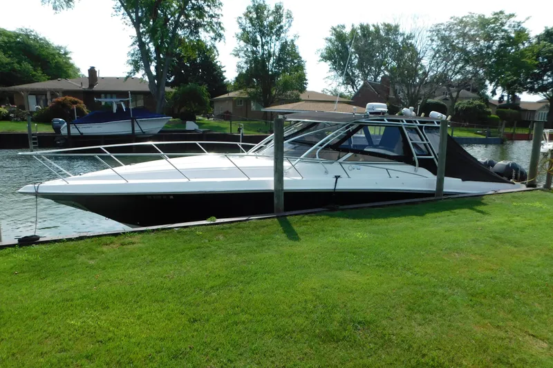 The Image of 2006 Fountain 38 LX boat docked by a grassy waterfront, surrounded by trees and houses. - 1