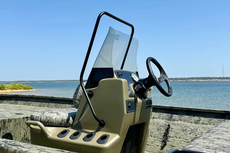 Slide: The Image of 2026 Tracker Grizzly 2072 CC boat console with steering wheel, near serene lake. - 13