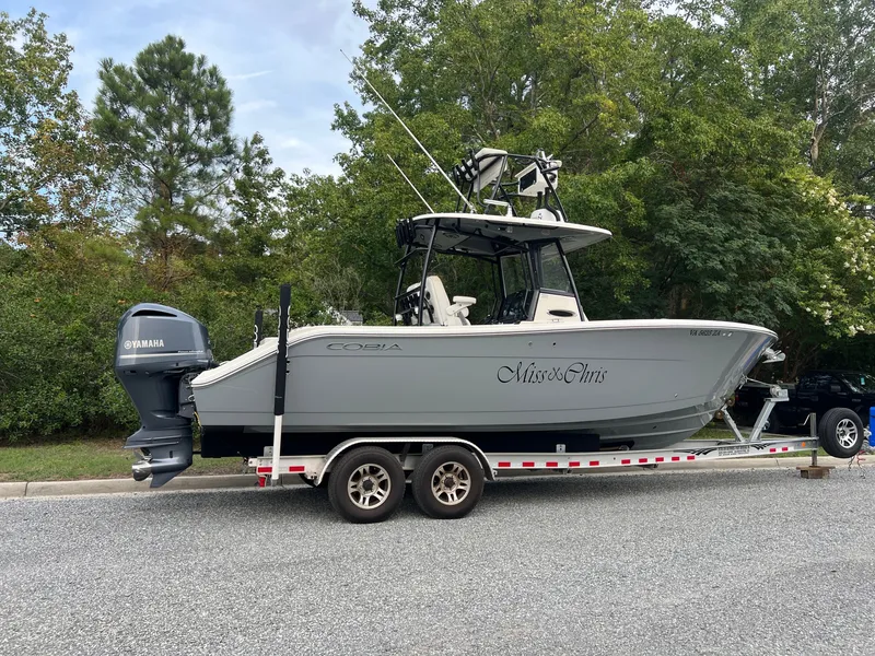 Slide: The Image of A 2020 Cobia 280 Center Console boat on a trailer, surrounded by trees. - 1