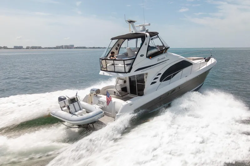 Slide: The Image of 2006 Sea Ray 455 Sedan Bridge cruising on open water, with a small boat attached. - 37