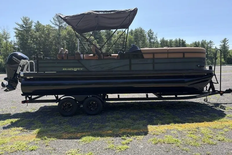 Slide: The Image of 2026 Ranger 220FC pontoon boat on trailer, parked outdoors with trees in background. - 3