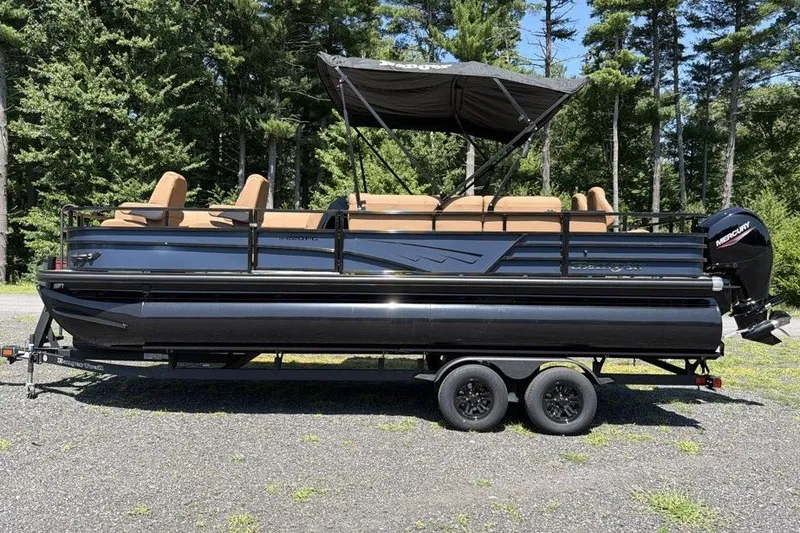Slide: The Image of 2026 Ranger 220FC pontoon boat on trailer, parked outdoors with forest background. - 1