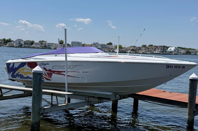The Image of 2002 Baja 25 Outlaw speedboat docked by waterfront homes under a clear blue sky. - 3