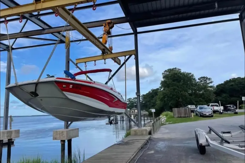 Slide: The Image of 2021 Crownline Eclipse E205 XS boat suspended on a lift by a lakeside dock. - 2