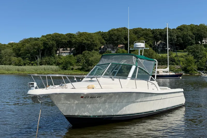 Slide: The Image of 1998 Pursuit 2860 Denali boat anchored on a calm lake with lush green shoreline. - 5