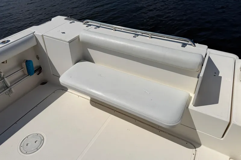 Slide: The Image of 1998 Pursuit 2860 Denali boat seating area with white cushioned bench by the water. - 6