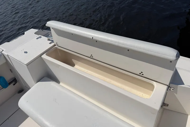 Slide: The Image of 1998 Pursuit 2860 Denali boat with open storage compartment, white seating, and water backdrop. - 9