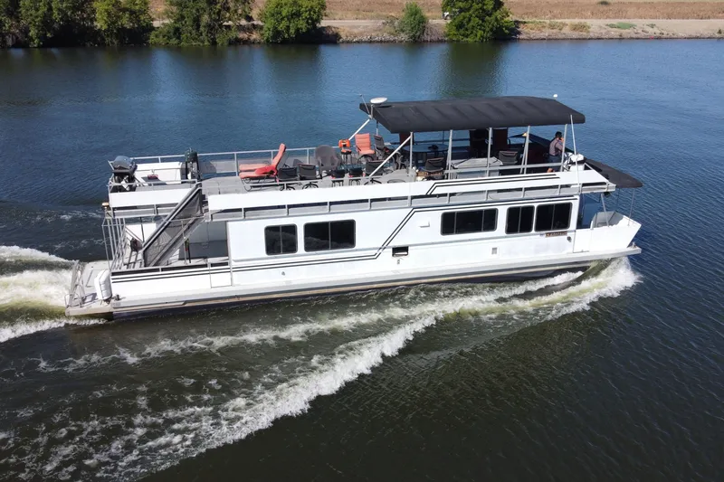 The Image of A 1998 Patio Cruiser 55 houseboat navigating a serene river, surrounded by lush greenery. - 0
