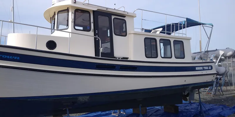 Slide: The Image of A 2001 Nordic Tug 32 is on a dry dock. It features a blue and white color scheme. - 2