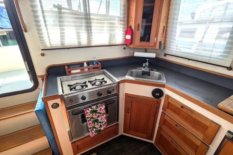 Slide: The Image of Cozy kitchen in a 2001 Nordic Tug 32 boat with stove, sink, and wooden cabinetry. - 28