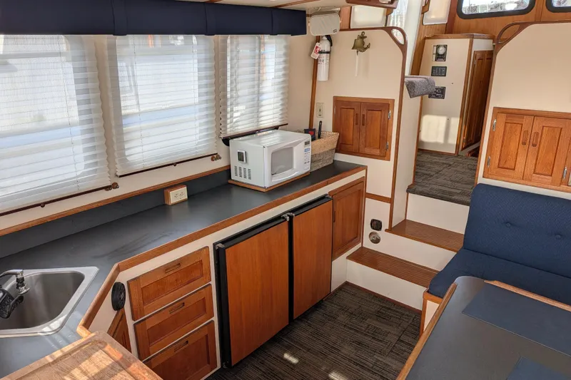 Slide: The Image of Interior of a 2001 Nordic Tug 32, featuring a compact kitchen with wooden cabinetry. - 23