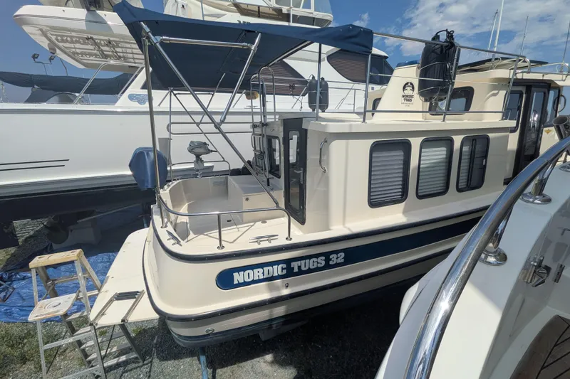 Slide: The Image of 2001 Nordic Tug 32 boat with blue canopy, docked alongside other vessels. - 8