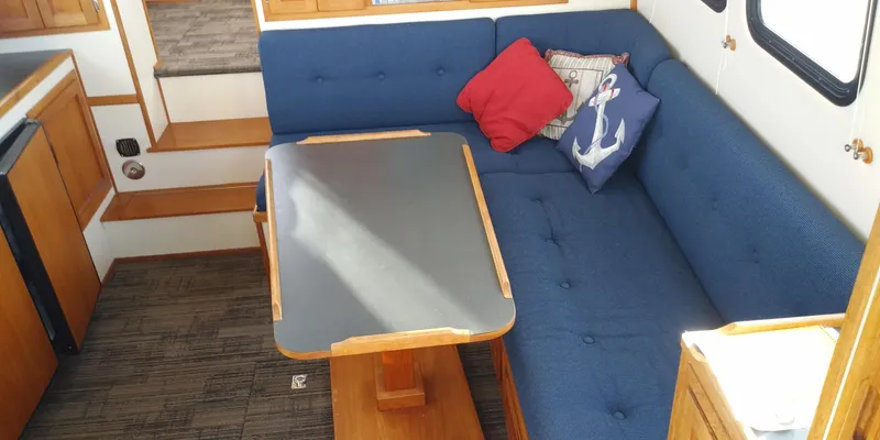 Slide: The Image of Interior of a 2001 Nordic Tug 32 with blue upholstery and a wooden table. - 18